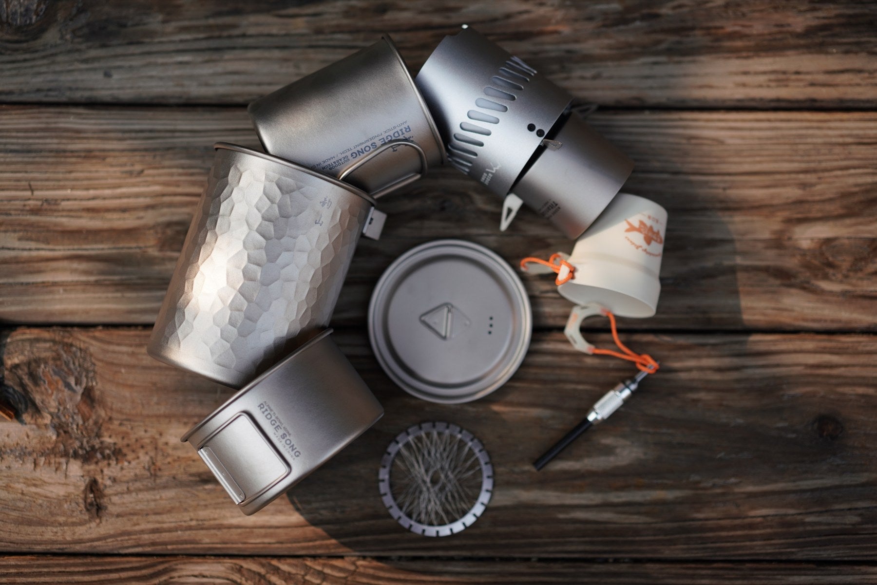 The pot, mug, stove, bowl and a sharing cup arranged together on a wooden table