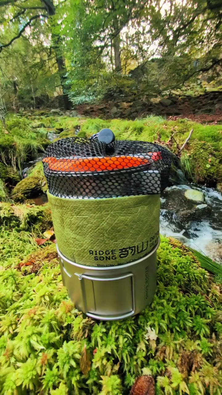 The packed cookware system resting on moss beside a woodland stream