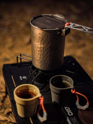 A hammered titanium pot beside two small cups at an outdoor evening tea setup.