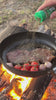 Steak cooking over fire and on a camp stove; no audio